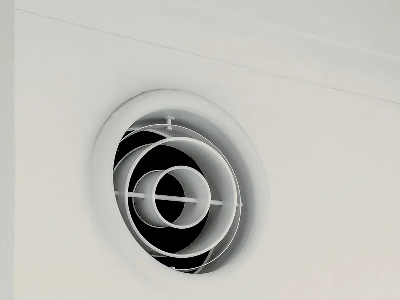 Runde weiße Abluftöffnung an einer hellen Wand unter der Decke